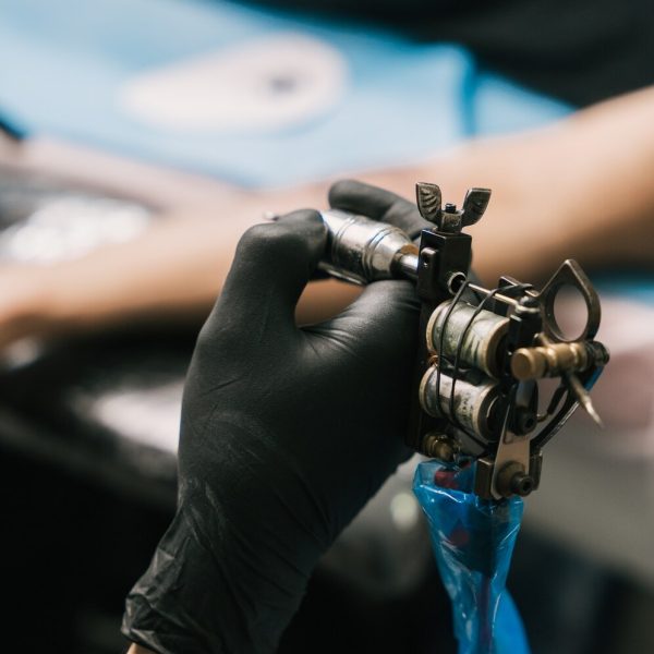 colpo-di-messa-a-fuoco-selettiva-della-mano-di-un-tatuatore-che-indossa-un-guanto-nero-e-che-tiene-una-pistola-per-tatuaggi_181624-21033